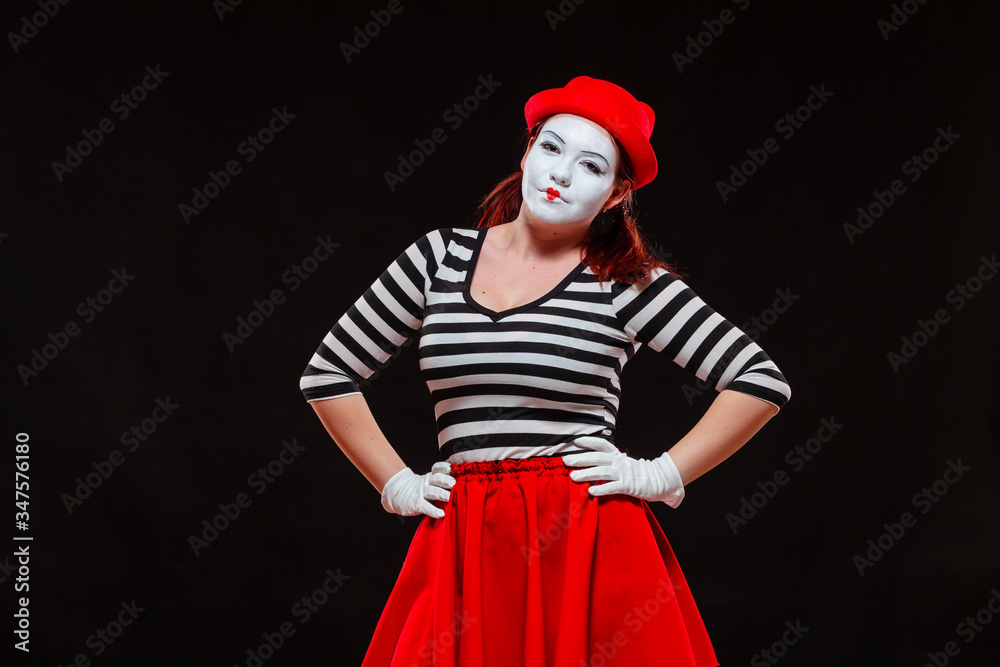 Portrait of female mime artist performing, isolated on black background. Woman in striped clothes and red skirt is standing with hands on her hips Portrait of female mime artist performing, isolated on black background. Woman in striped clothes and red skirt is standing with hands on her hips