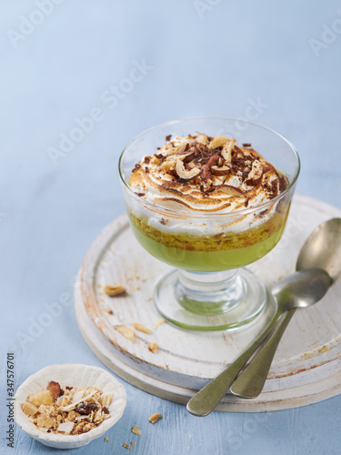 Matcha green tea panna cotta with coconut milk topped with hazelnut and burnt meringue on a light blue background in glass. Concept healthy gluten-free dessert for summer. Copy space, selective focus.