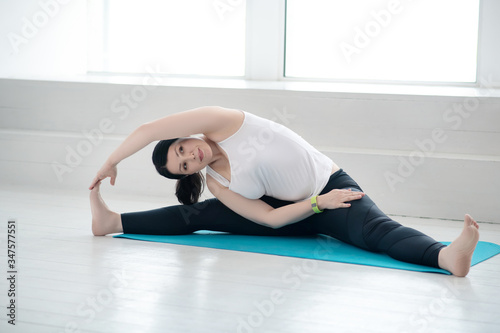 Brunette female sitting on rug, doing the splits, holding her big toe with one hand