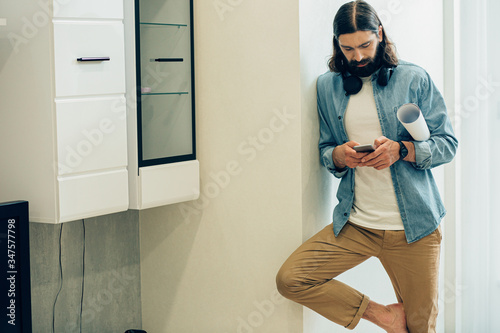 Calm man standing by the wall with smartphone in hands