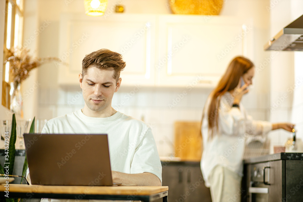 young caucasain married couple busy with their own business at home, man work on laptop from home while his wife make breakfast in the background. freelance, quarantine concept