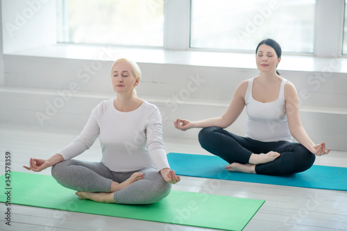 Brunette female and blonde female sitting in lotus pose, meditating