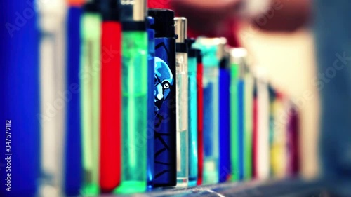 Cinemagraph of cartoon face of a man on blue lighter that looking at camera and blinking. He glances between many other lighters that are lined up. Closeup, loop, selective focus with copy space.