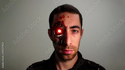 Cinemagraph of red light blinking from the eye of a cyborg humanoid man. Dramatic closeup portrait of a young bearded man with an expressionless face that looking at the camera.