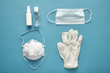 Coronavirus prevention disposable surgical masks, medical respirator, latex gloves, and pocket hand sanitizer gel for hand hygiene corona virus protection, top view on blue background.