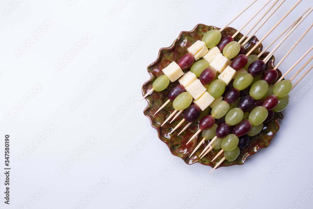 slices of cheese and grapes on a stick in a plate on a table slices of cheese and grapes on a stick in a plate on a table