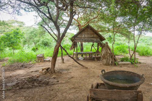 Myanmar Travel Images, Myanmar travel image of rustic stick and palm frond shelter in dirt patch under trees with washing stad with water bowl. © Brian Scantlebury