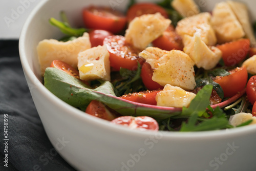 salad with cherry tomatoes, mixed grens and cheese in white bowl on concrete background photo