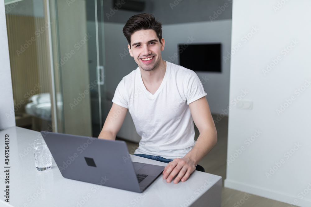 Young attractive smiling man is browsing at his laptop, sitting at home
