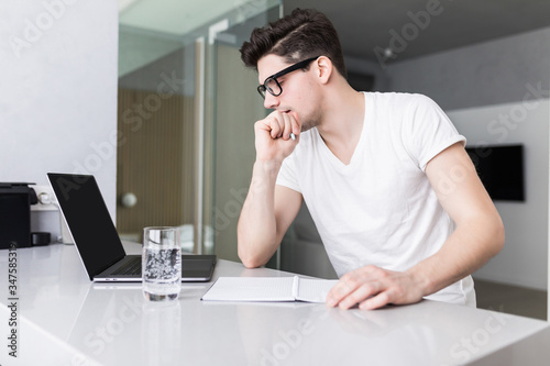 Young man sitting at home and looking at computer screen reading message email. Student studying learning online using laptop. Concentrated freelancer working at home on internet