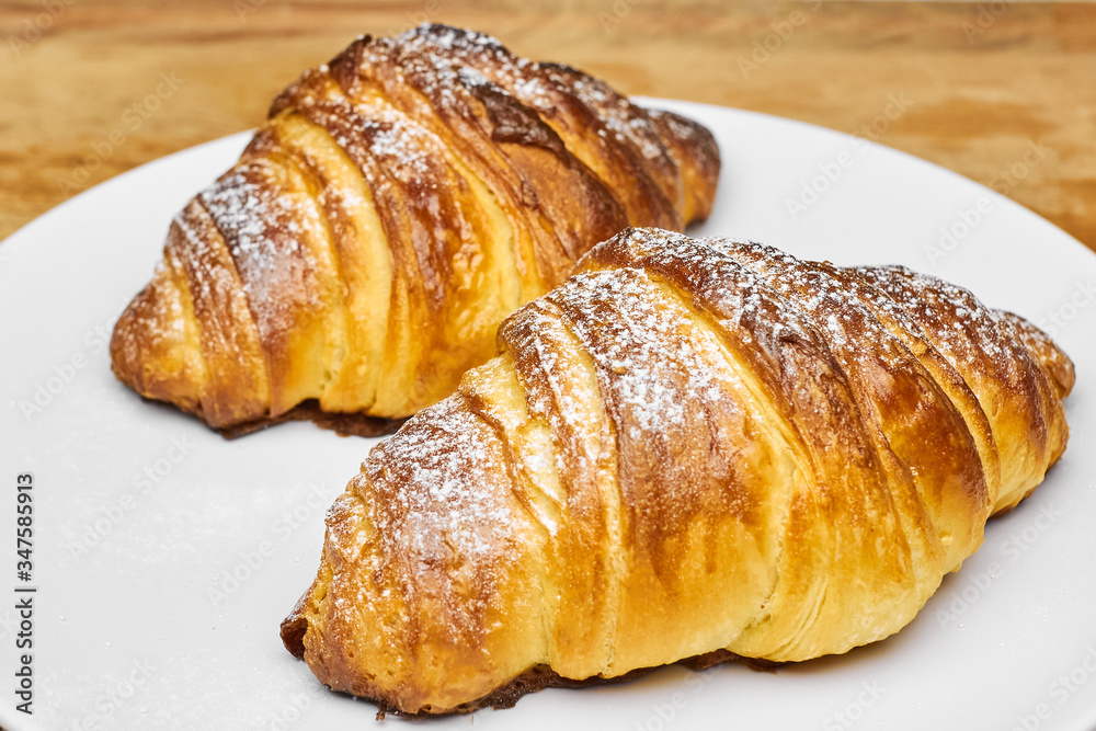Close up two freshly baked croissants with sugar powder on a white plate. Puff french pastry. 