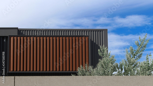 The back of a new townhouse. Pictured is the second storey showing balcony above garage. The structure is metal clad and there are brown exterior aluminium horizontal louver window coverings. Blue sky