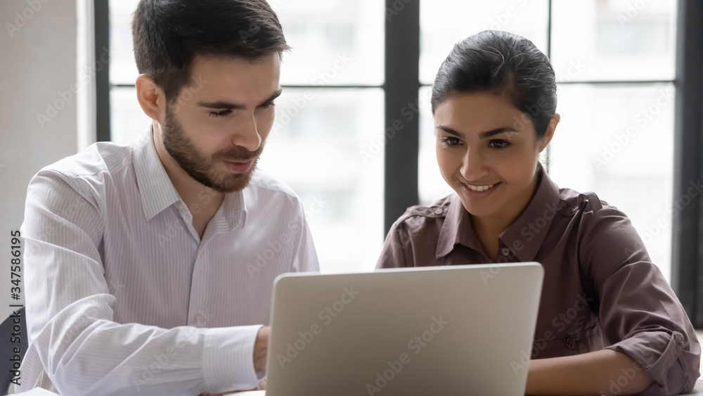 Diverse smiling businessman and businesswoman talking looking at laptop screen. Indian woman and male manager discuss and looking decision in negotiation. Teamwork at workplace concept. Diverse smiling businessman and businesswoman talking looking at laptop screen. Indian woman and male manager discuss and looking decision in negotiation. Teamwork at workplace concept.