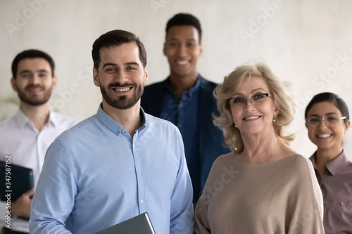 Close up headshot portrait of two happy businessman and mature businesswoman looking at camera. Diverse smiling employee standing behind of female and male company mentors. Leader of multi-ethnic team