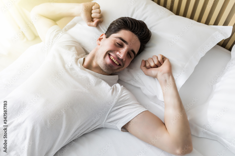 Young handsome happy man waking up on bed, top view - obrazy, fototapety, plakaty 