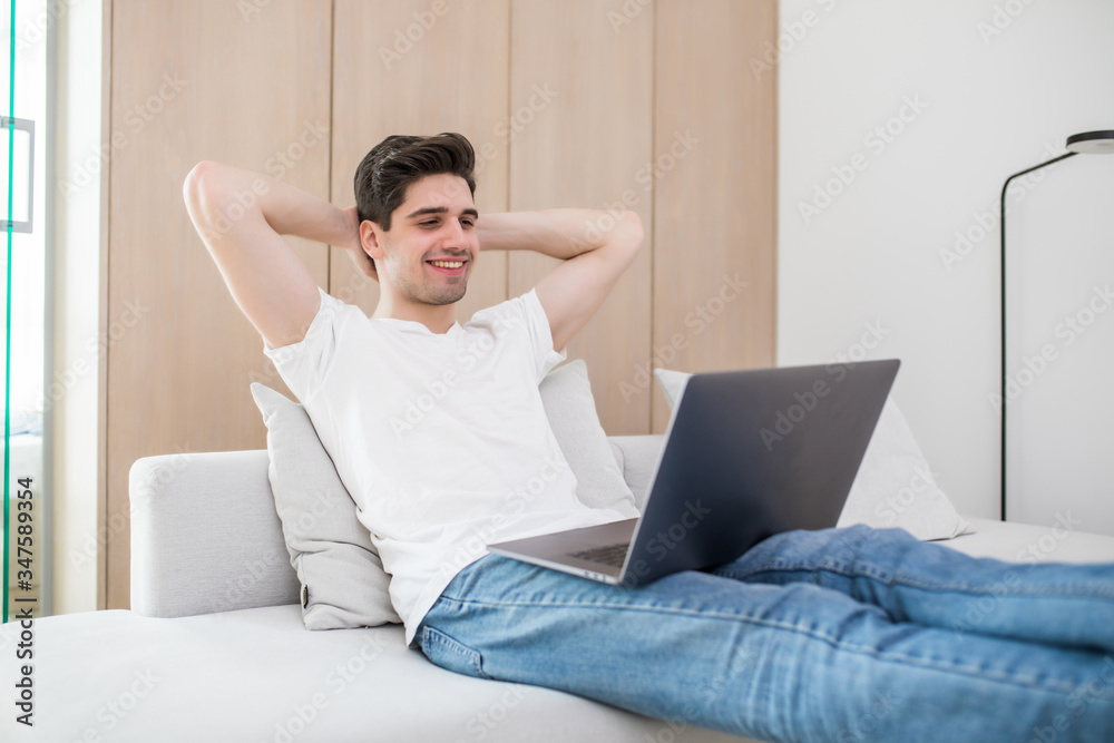 Handsome man is holding hands behind head and smiling while working with a laptop at home Handsome man is holding hands behind head and smiling while working with a laptop at home