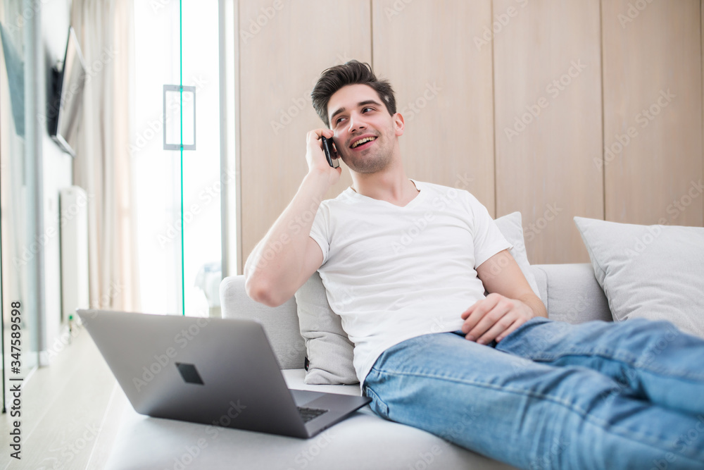 Young man using a laptop while talk on the phone sitting on the couch Young man using a laptop while talk on the phone sitting on the couch