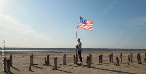 The American patriot rides a gyroboard along wooden piles holding a flagpole with a fluttering USA flag.