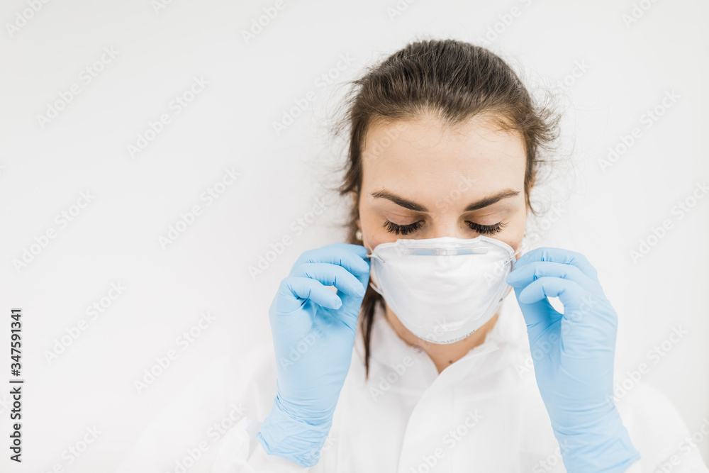 The girl doctor puts on a white protective medical mask in blue gloves on a white background.