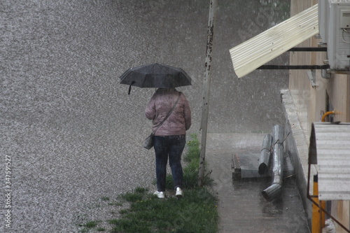 Fotografi A woman under an umbrella stands near a house with a collapsed drainpipe on the