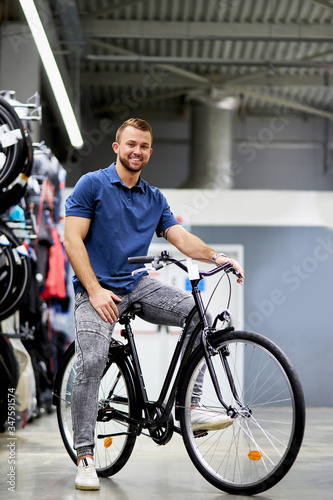 portrait of young handsome guy sitting on new bicycle in sportswear store, going to buy, look at camera and smile