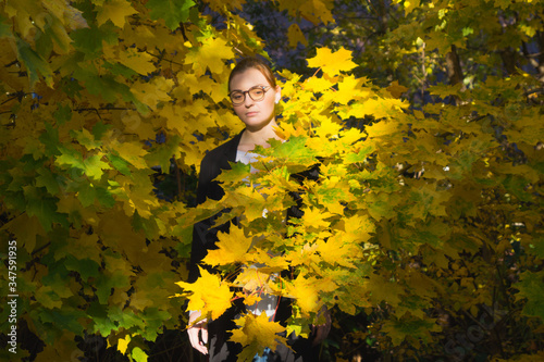 A woman is standing among vibrant yellow and green foliage looking sad and thoughtful.