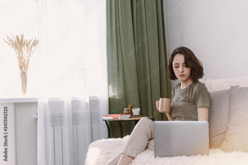 Beautiful young woman working on laptop computer while sitting at home, drinking coffee Beautiful young woman working on laptop computer while sitting at home, drinking coffee
