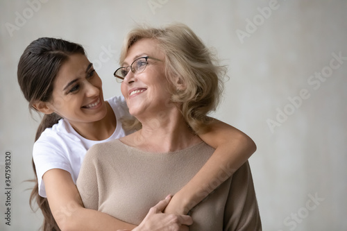 Fototapeta Close up headshot portrait picture of adult daughter hugs from behind happy mature mother enjoying tender moment looking at each other