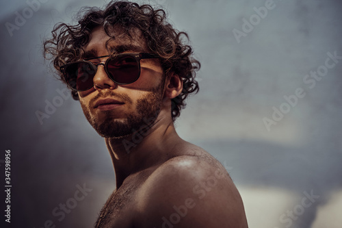 Handsome young adult man isolated in a dark studio, posing shirtless wearing sunglasses