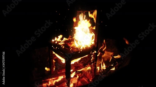 Cinemagraph of wooden chair burning inside the bonfire. Close up on sparks rises from the fire with heatwaves at night. A horror concept of a demonic ritual or devil and demons religious worship.