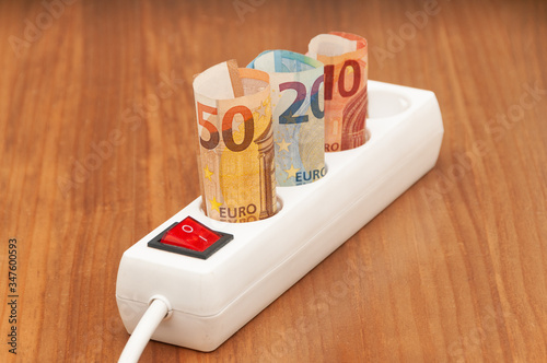 Euro banknotes inserted into an extension socket on a wooden surface. Expensive concepts of energy and cost of electricity. Front view.