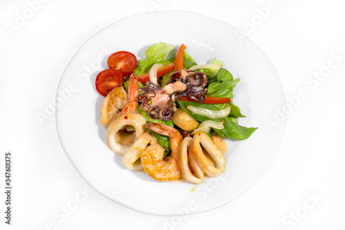 Seafood appetizer on a white plate on a white background. Small octopuses, king prawns, squid rings decorated with cherry tomatoes and herbs
