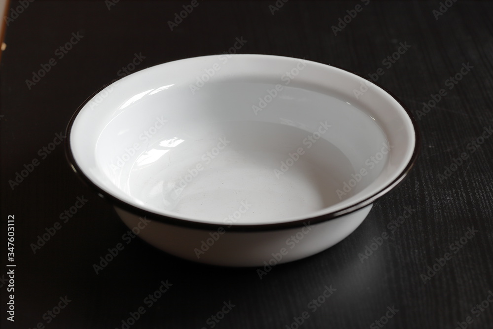 a white enameled empty clean bowl stands on a dark table against a black background a white enameled empty clean bowl stands on a dark table against a black background