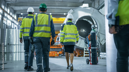 Shot of Heavy Industry Engineers and Workers Walking through Pipe Manufacturing Factory. Modern Facility for Design and Construction of Oil, Gas and Fuels Transport Pipeline.