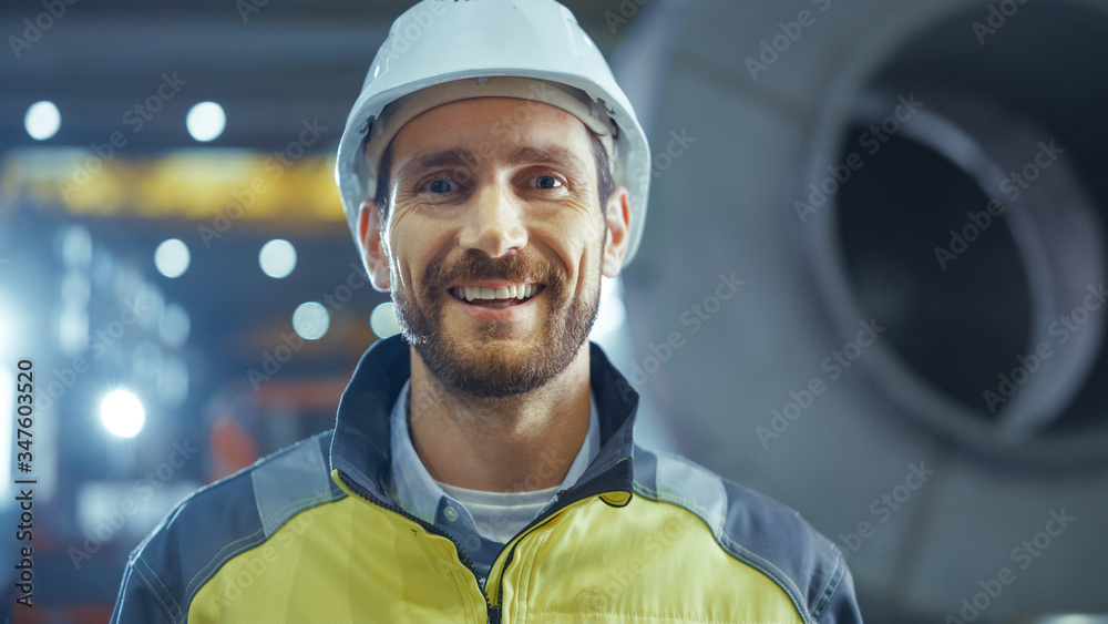 Portrait of Smiling Professional Heavy Industry Engineer / Worker Wearing Safety Uniform and Hard Hat. In the Background Unfocused Large Industrial Factory - obrazy, fototapety, plakaty 