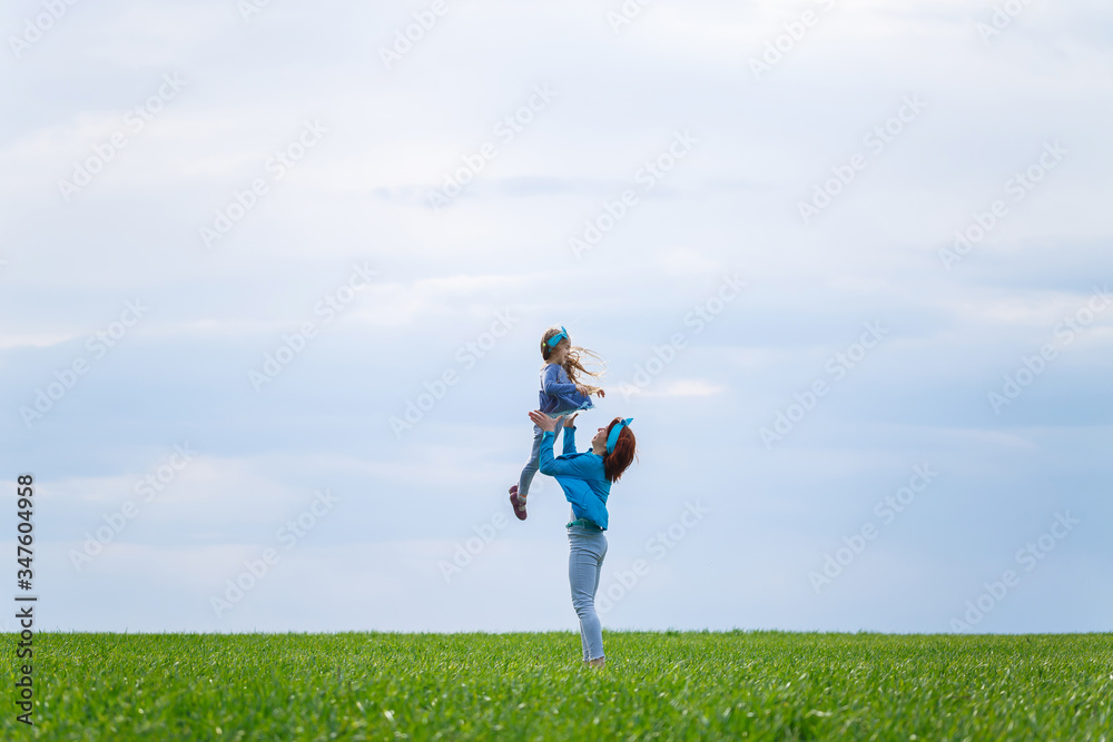 little girl child and mother woman run and jump, green grass in the field, sunny spring weather, smile and joy of the child, blue sky with clouds little girl child and mother woman run and jump, green grass in the field, sunny spring weather, smile and joy of the child, blue sky with clouds