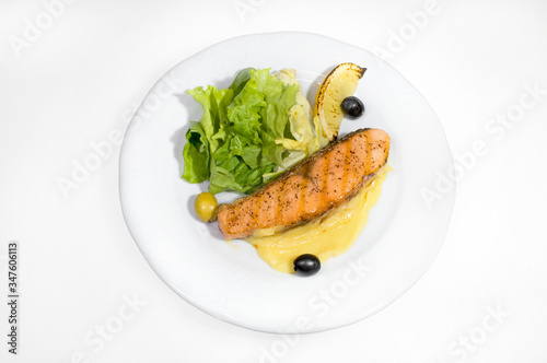 Fried piece of salmon with mashed potatoes and lettuce leaves decorated with olives and lemon idol on a white plate on a white plate