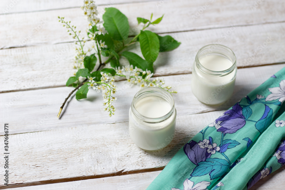 Home made yogurt in glass jars  on textile cover on white wooden background with bird cherry branch