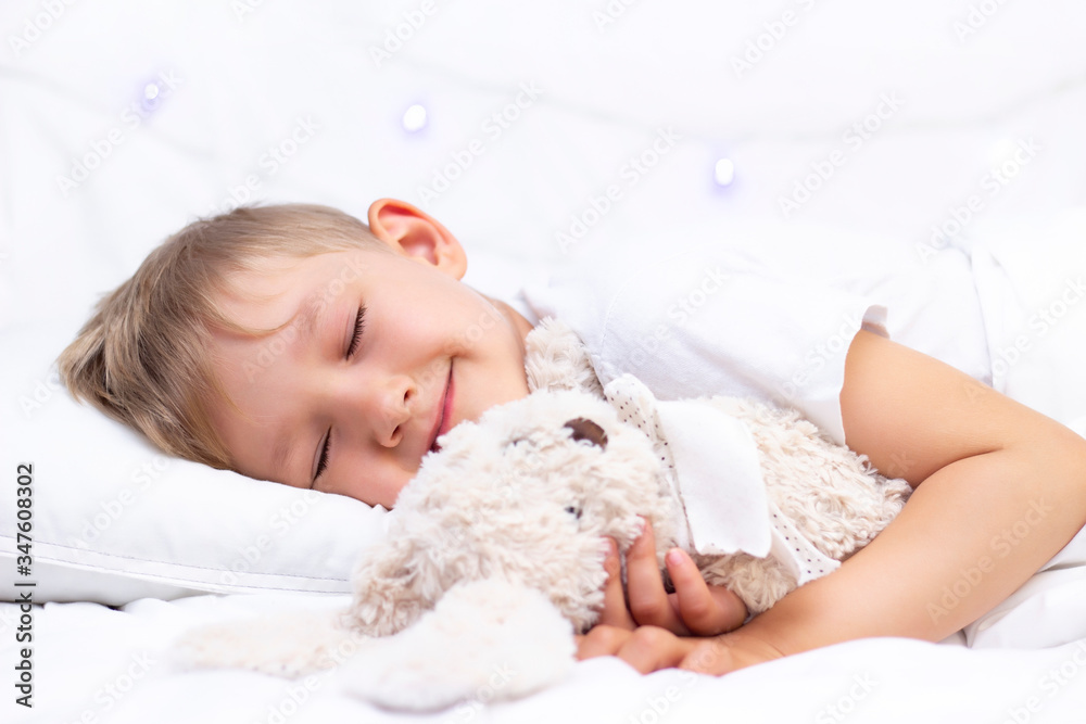 Charming little white boy sleeps in bed. hugs a soft toy Charming little white boy sleeps in bed. hugs a soft toy