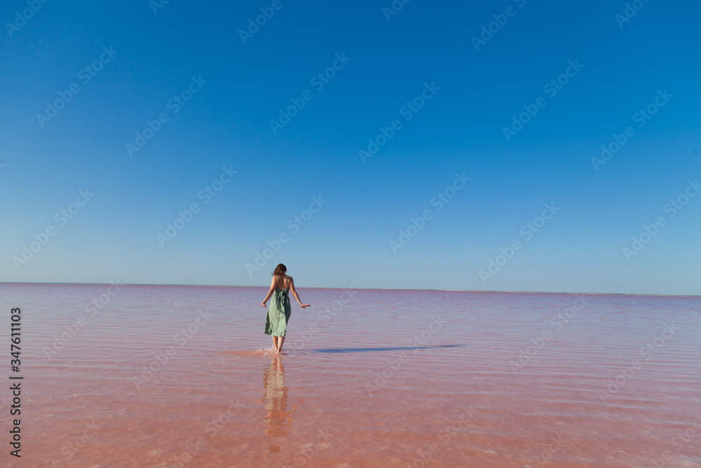 Woman in dress stands in rose water lake against blue sky