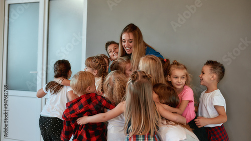 Young and happy female dance teacher hugging children and smiling while standing in studio. Relationship between teacher and kids. Choreography class
