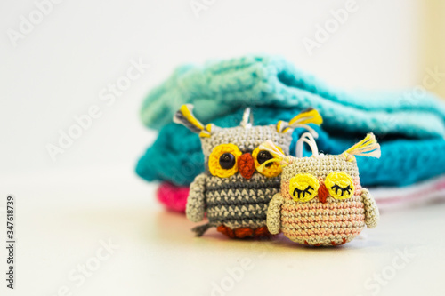 Two small multi-colored knitted handmade owl toys sits against a white background. Amigurumi. Blurred color background.