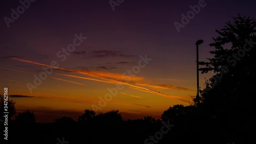 Night to day timelapse of winter sunrise over silhouette of trees and street light switching off in England