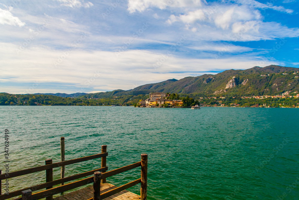 Vista del Lago d'Orta, Piemonte, Italia, con le montagne sullo sfondo e cielo blu con nuvole bianche.