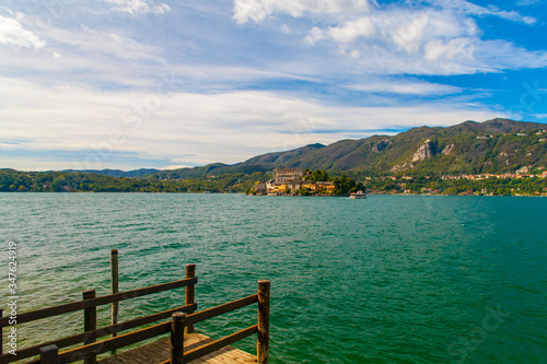 Vista del Lago d'Orta, Piemonte, Italia, con le montagne sullo sfondo e cielo blu con nuvole bianche.