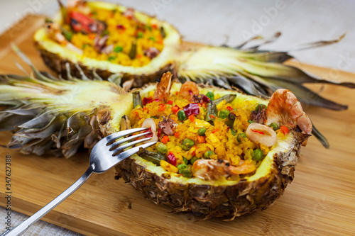 Photo two pineapple halves with rice and seafood on wooden background, view from the t