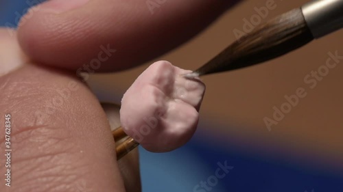Dental technician applies ceramic material to the crown of a dental implant in a dental laboratory using tweezers and a brush. Dental technology close-up. photo