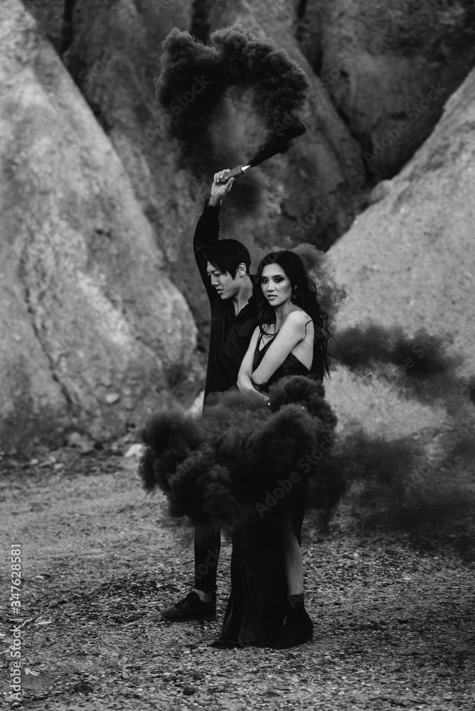 An Asian couple in love lit black smoke bombs in the mountains. Colored smoke. Black-white An Asian couple in love lit black smoke bombs in the mountains. Colored smoke. Black-white