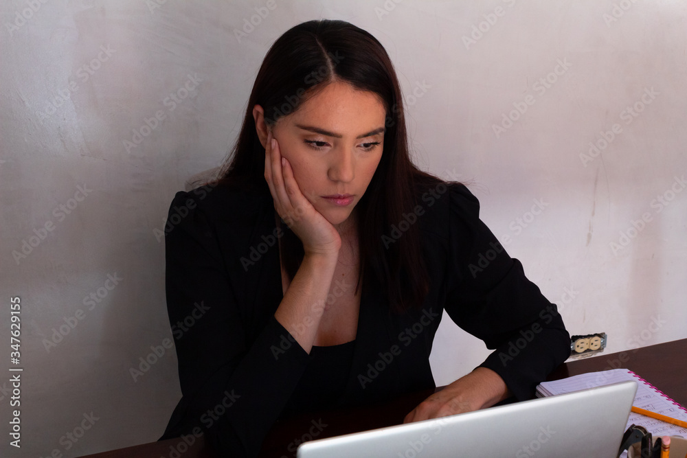 Young Hispanic woman in black clothes doing home office with a white laptop, bored and stressed from work Young Hispanic woman in black clothes doing home office with a white laptop, bored and stressed from work