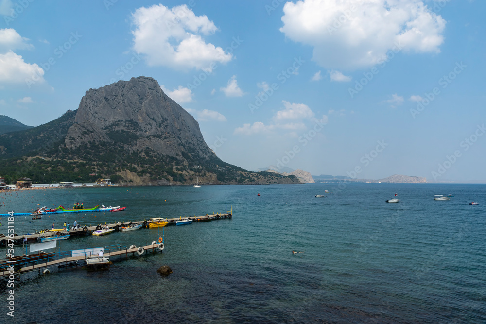 Sudak, New World, Russia - July 29, 2016: Panoramic view of the Black Sea coast. A pier with boats in the bay, view of Mount Sokol.